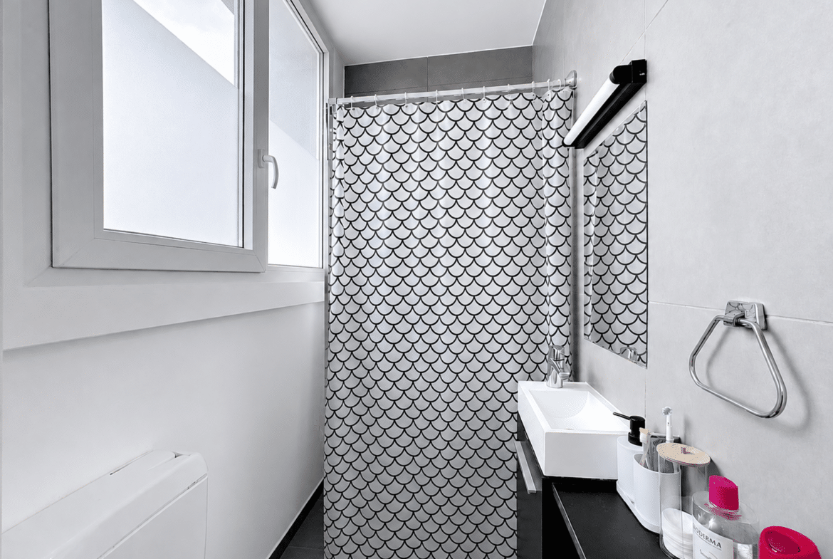 Salle de bain moderne d’appartement avec meuble vasque noir et rideau graphique.