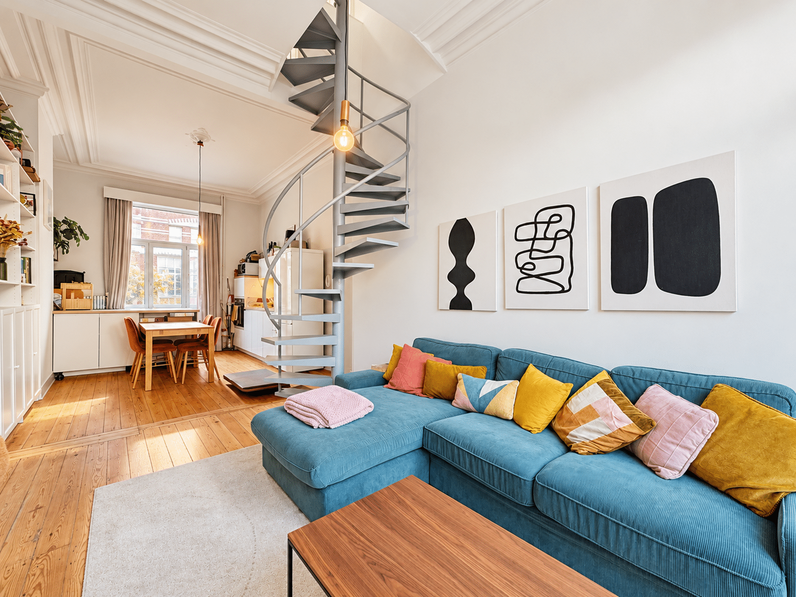 Woonkamer met wenteltrap – You Real Estate Agency Licht appartement met een blauwe woonkamer, een open keuken en een wenteltrap.