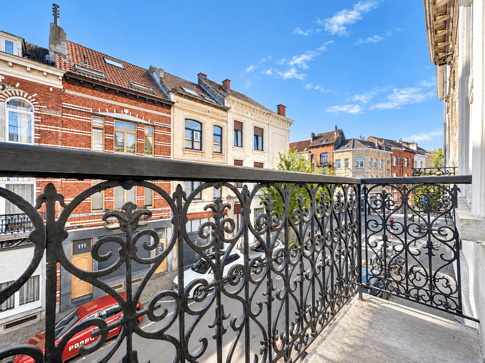 Balkon met uitzicht op een rustige woonstraat – You Real Estate Agency Balkon van een appartement met uitzicht op een woonstraat en karakteristieke huizen.
