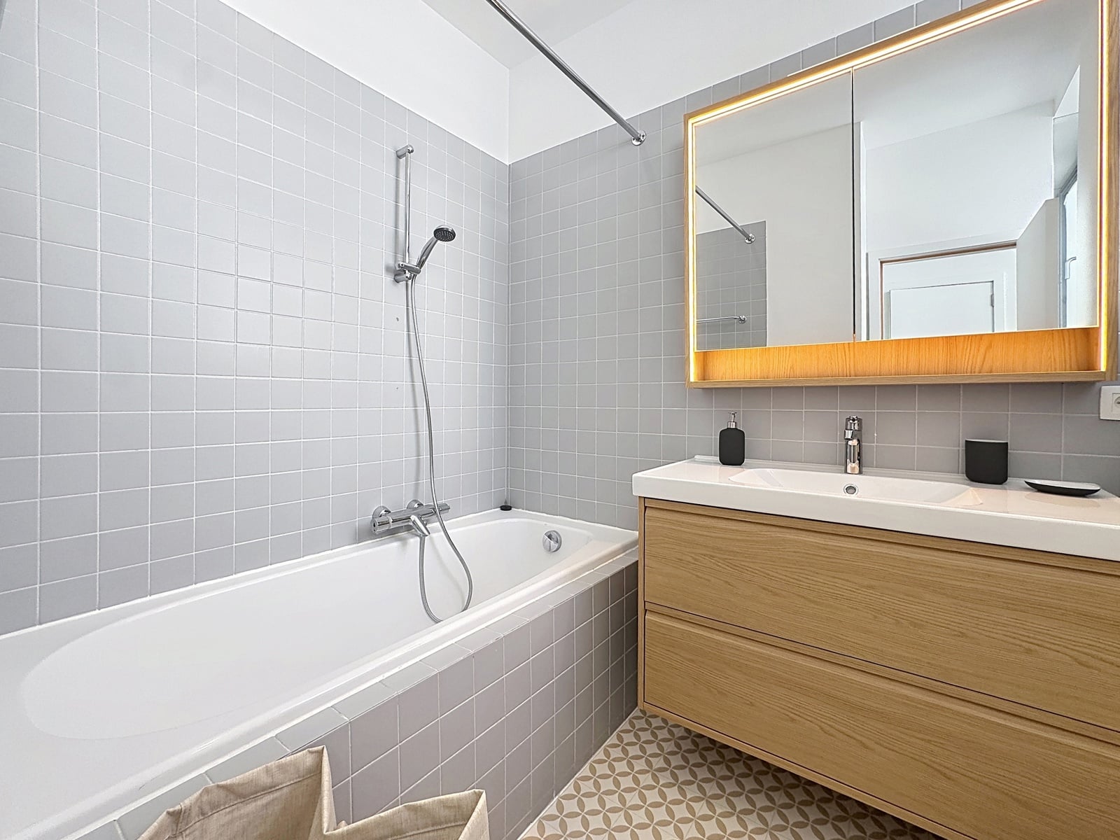 whise photo 8 Modern bathroom with bathtub, gray tiled walls, and wooden vanity with a backlit mirror.