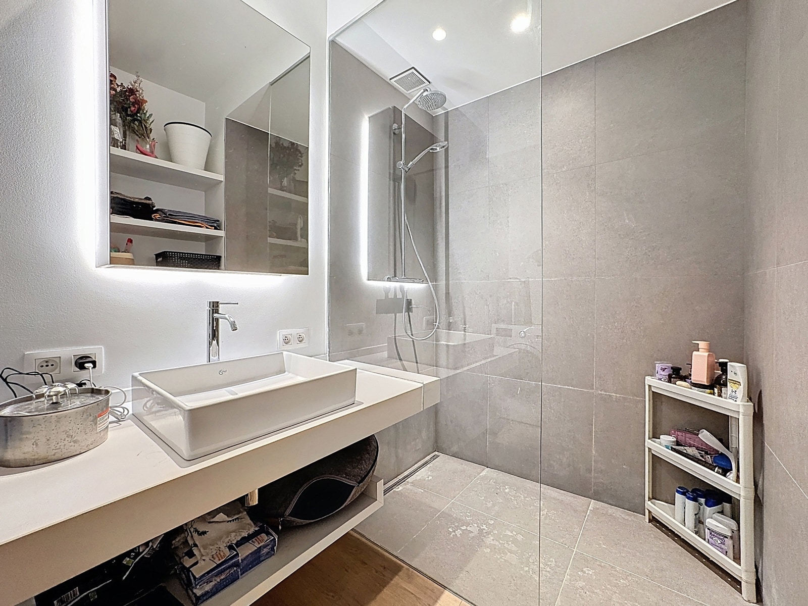 whise photo 9 Modern bathroom with a white countertop sink, backlit mirror, and glass shower enclosure on gray tiled walls.