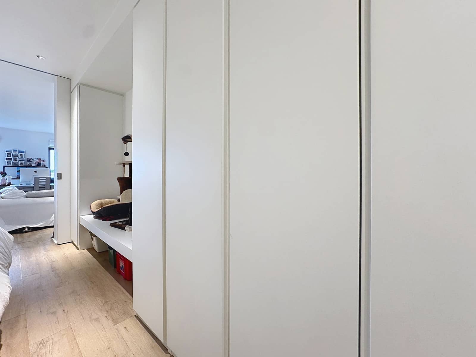 whise photo 8 White built-in wardrobes line a bright hallway, with an open shelf showing a hat and cushions and a bedroom visible to the left.