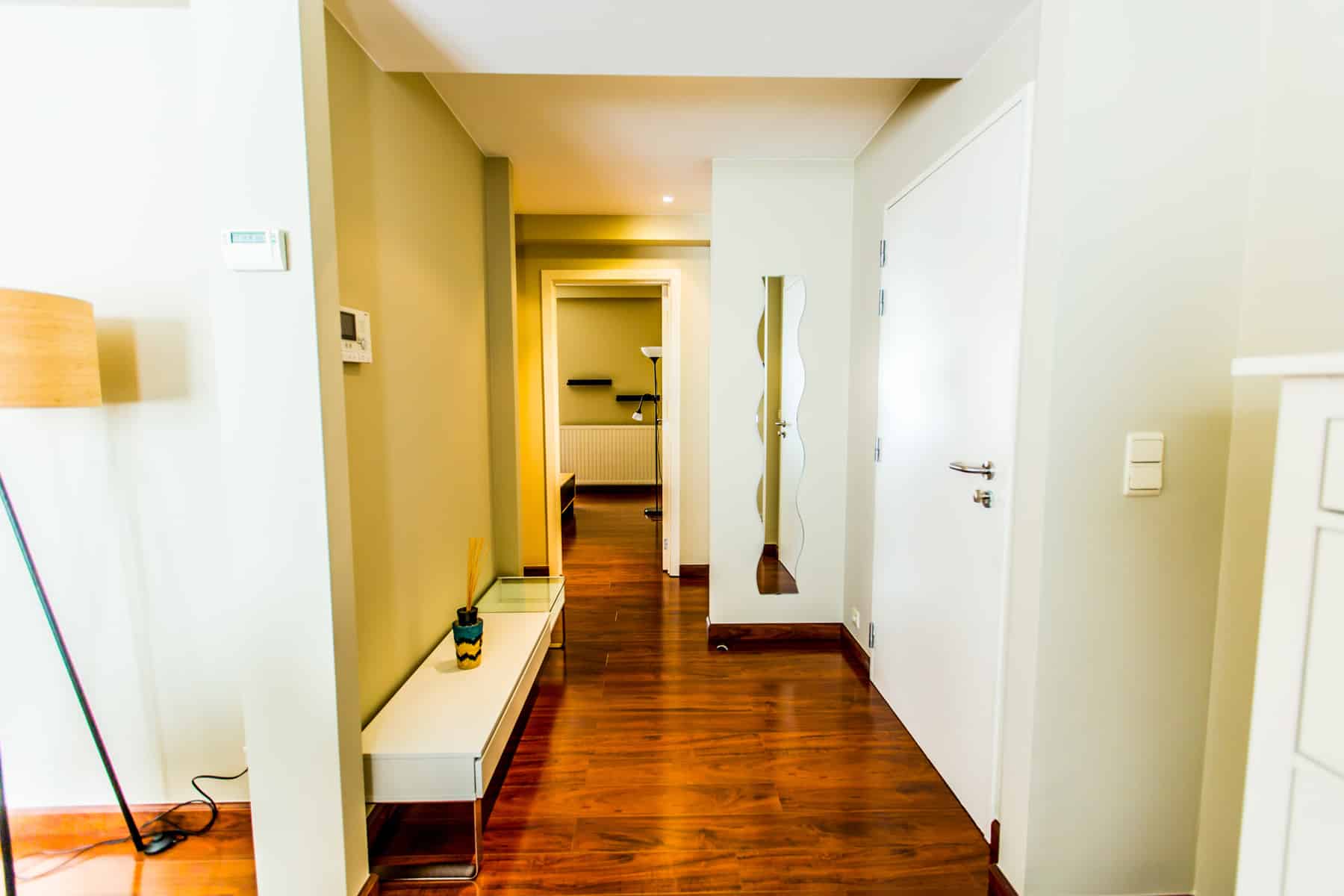 whise photo 7 A bright hallway with a wooden floor, white doors, and a curved mirror on the right; warm light at the far end.