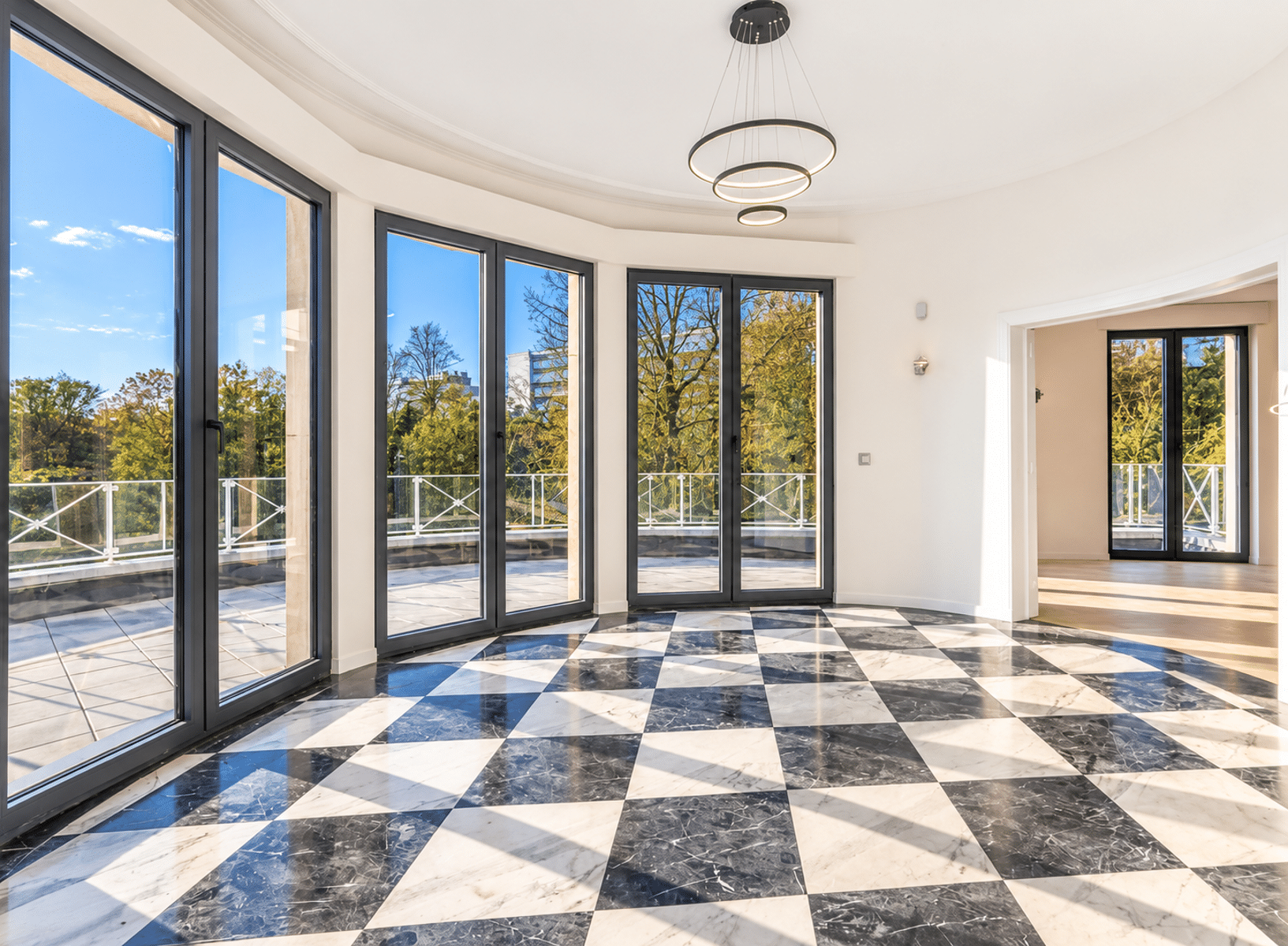 whise photo 5 Bright, modern interior with tall black-framed glass doors opening to a balcony and a black-and-white marble checkerboard floor.