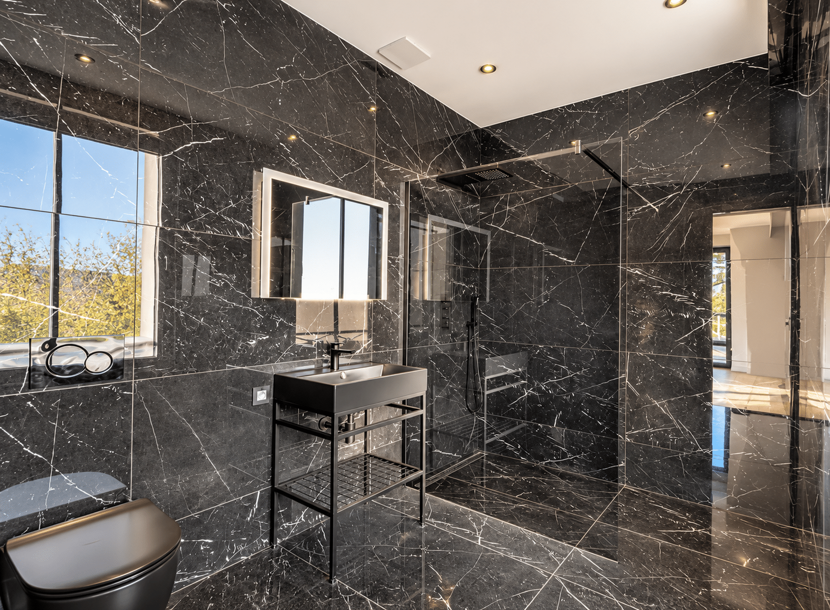 Salle de Bain en Marbre Noir – You Real Estate Agency Salle de bain moderne en marbre noir avec douche italienne et fenêtre lumineuse.