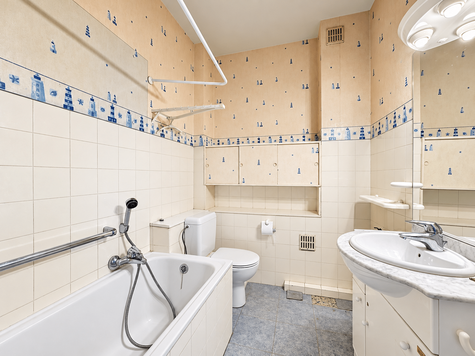 Salle de Bain Nautique Lumineuse – You Real Estate Agency Salle de bain lumineuse avec baignoire, douche, WC et meuble vasque d’appartement.