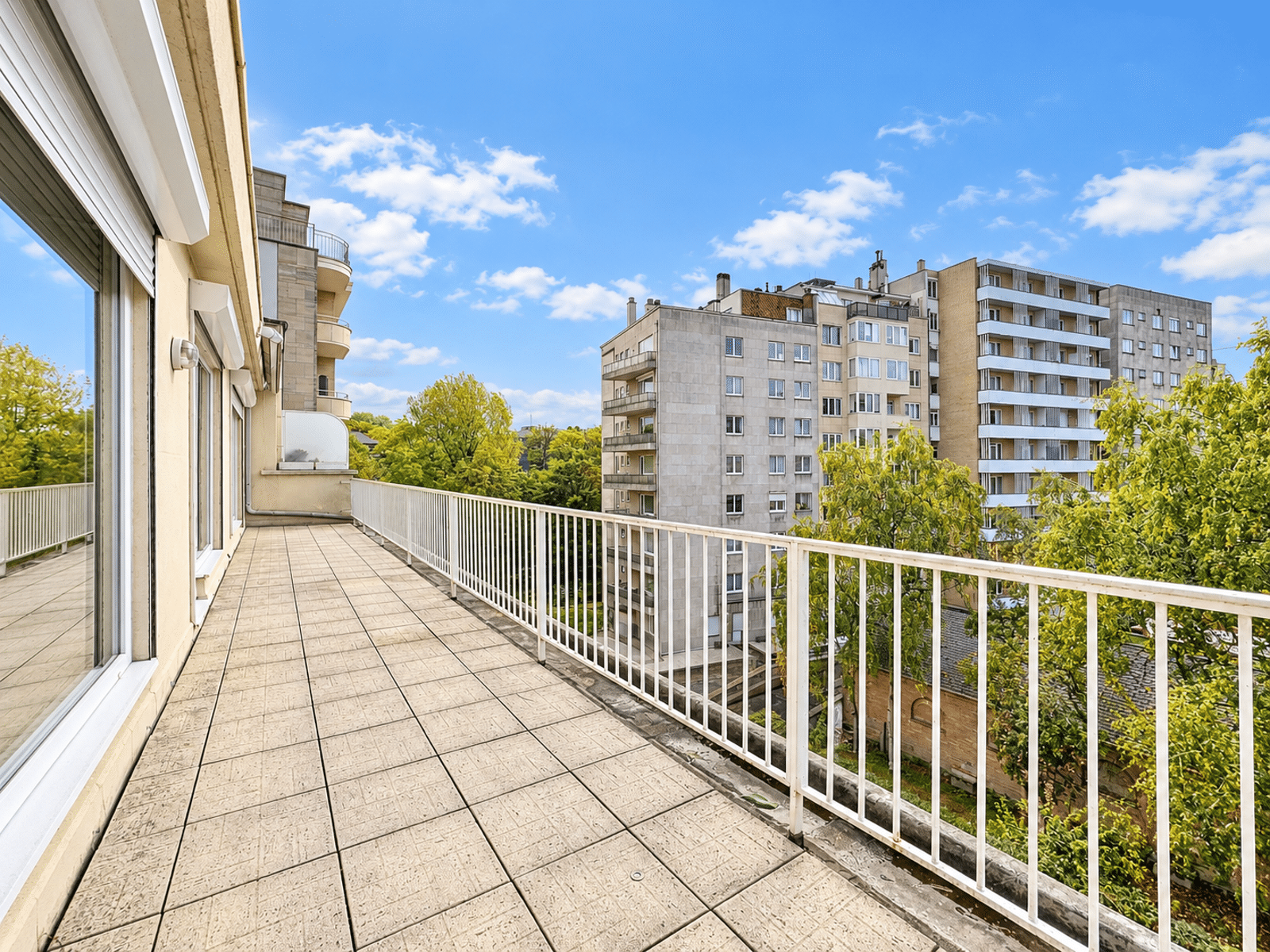 Terrasse Spacieuse avec Vue Arborée – You Real Estate Agency Grande terrasse d’appartement avec garde-corps blanc et vue arborée.