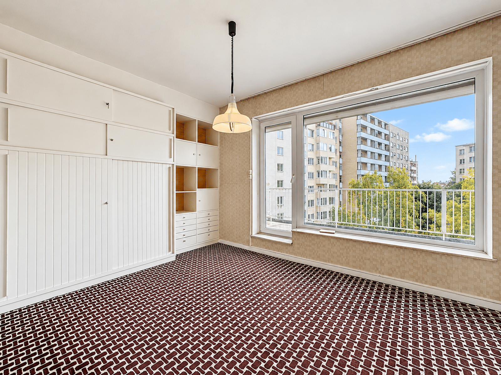 Pièce Lumineuse avec Placards Intégrés – You Real Estate Agency Pièce lumineuse d’appartement avec rangements intégrés, grande fenêtre et moquette vintage.