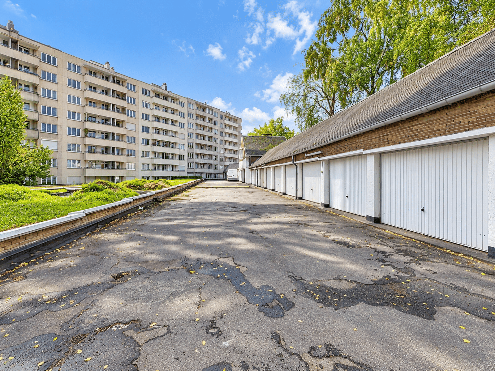 Cour Intérieure avec Garages – You Real Estate Agency Cour intérieure résidentielle avec garages et immeuble d’appartements ensoleillé.