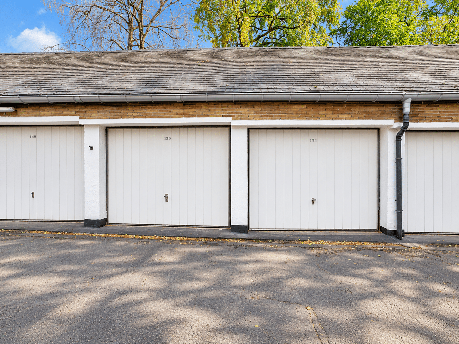 Rangée de Garages Privatifs – You Real Estate Agency Rangée de garages privatifs attenants avec portes blanches et toiture inclinée.