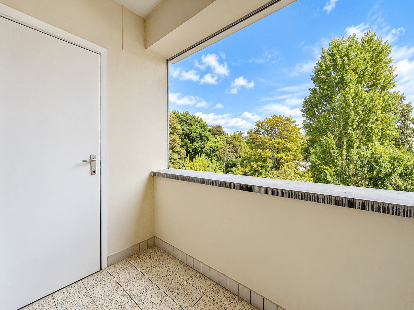 Terrasse Couverte avec Vue Verdoyante – You Real Estate Agency Terrasse couverte d’appartement avec vue verdoyante et sol carrelé.