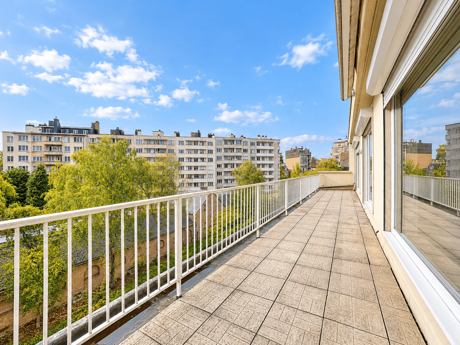 Terrasse Spacieuse avec Vue Urbaine – You Real Estate Agency Terrasse d’appartement spacieuse avec vue urbaine et garde-corps blanc.