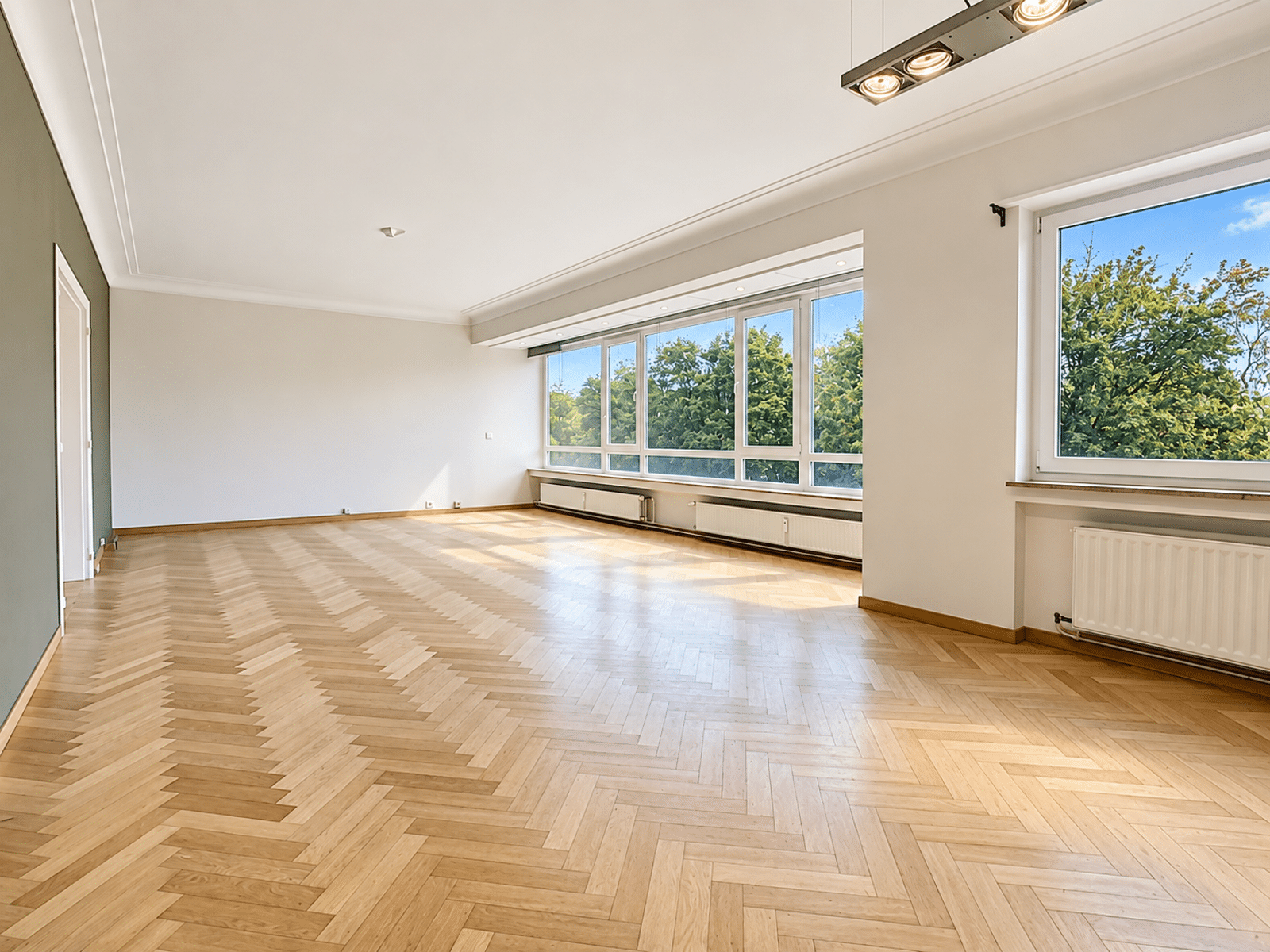 Salon Lumineux au Parquet Chevrons – You Real Estate Agency Grand salon lumineux avec parquet en chevrons et grandes fenêtres.