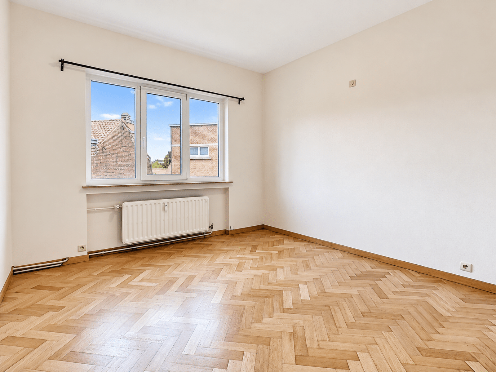 Pièce Lumineuse Parquet Chevrons – You Real Estate Agency Pièce lumineuse d’appartement avec parquet en chevrons et grande fenêtre.