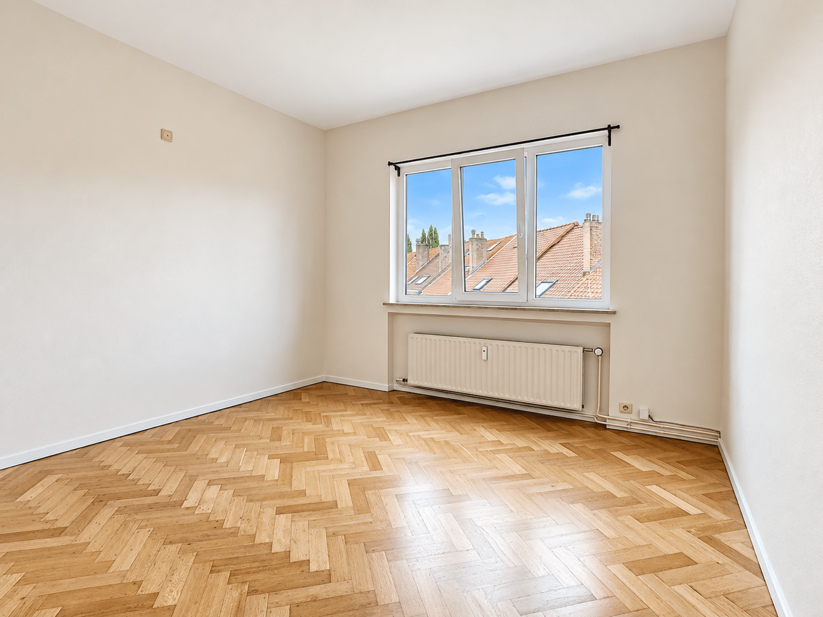 Pièce Lumineuse avec Parquet – You Real Estate Agency Pièce lumineuse d’appartement avec parquet en chevrons et vue sur les toits.