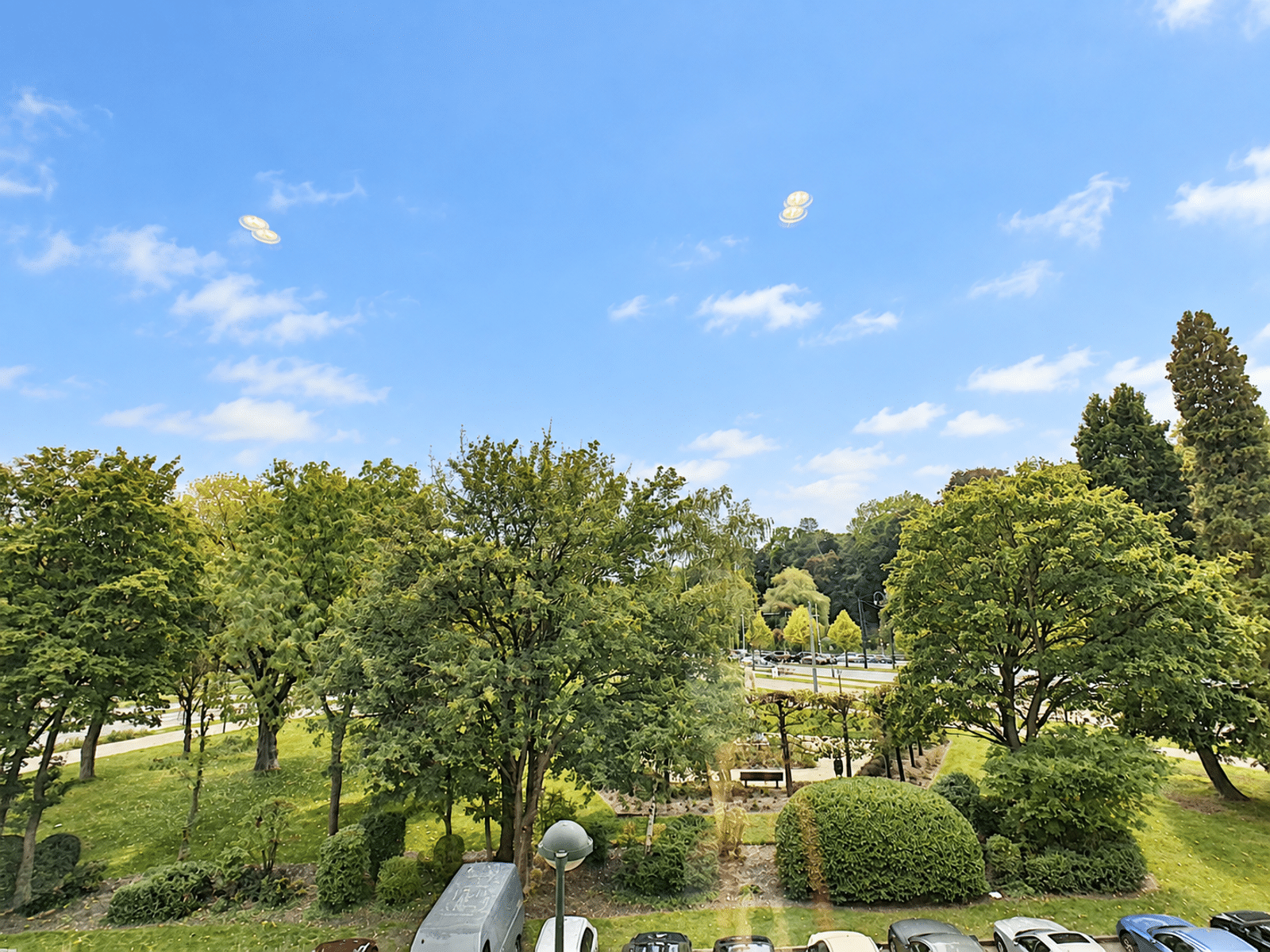 Vue Sur Jardin Paysager – You Real Estate Agency Vue verdoyante depuis appartement sur jardin paysager et parking résidentiel.