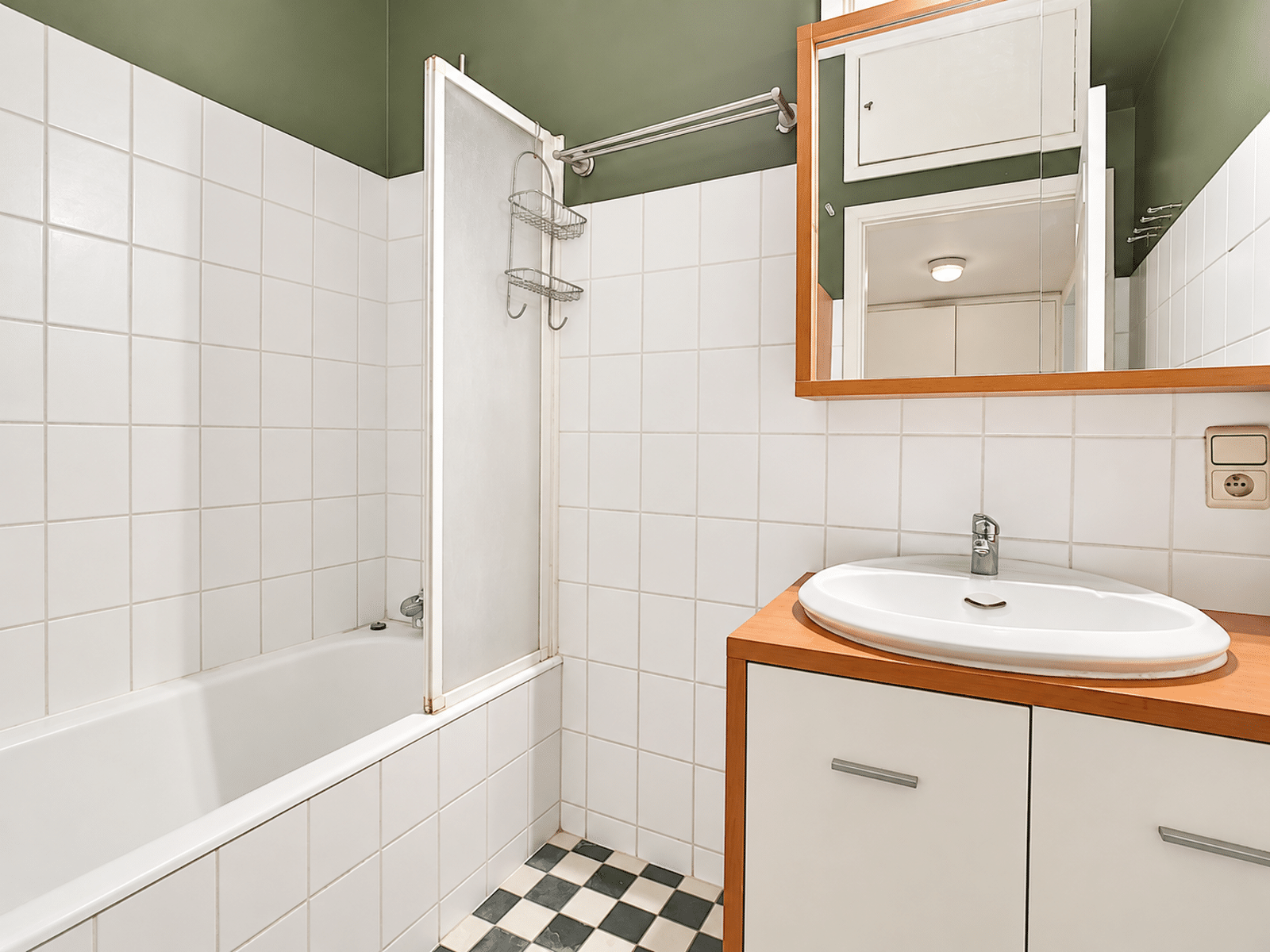 Salle de Bain Compacte avec Baignoire – You Real Estate Agency Salle de bain compacte d’appartement avec baignoire, vasque et carrelage noir et blanc.