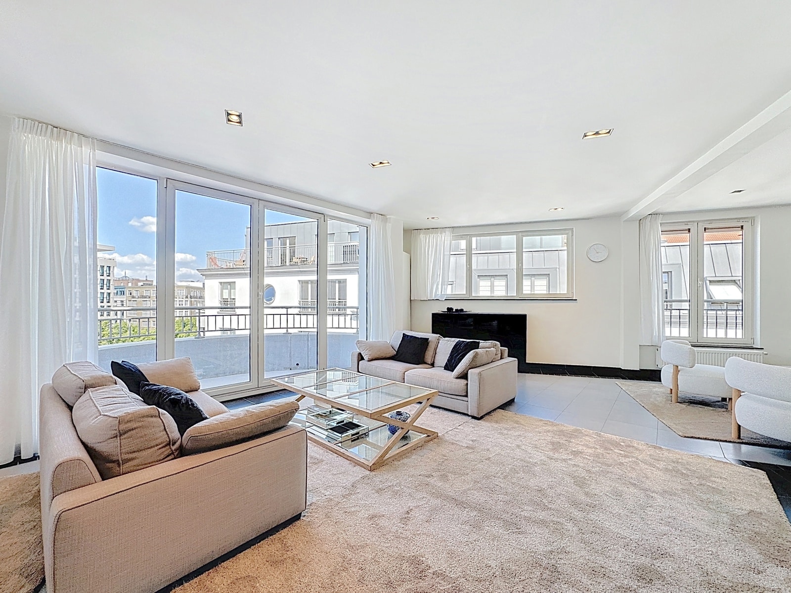 Salon Moderne Avec Vue Urbaine – You Real Estate Agency Salon lumineux d’appartement moderne avec grandes fenêtres, canapés beiges et vue urbaine.