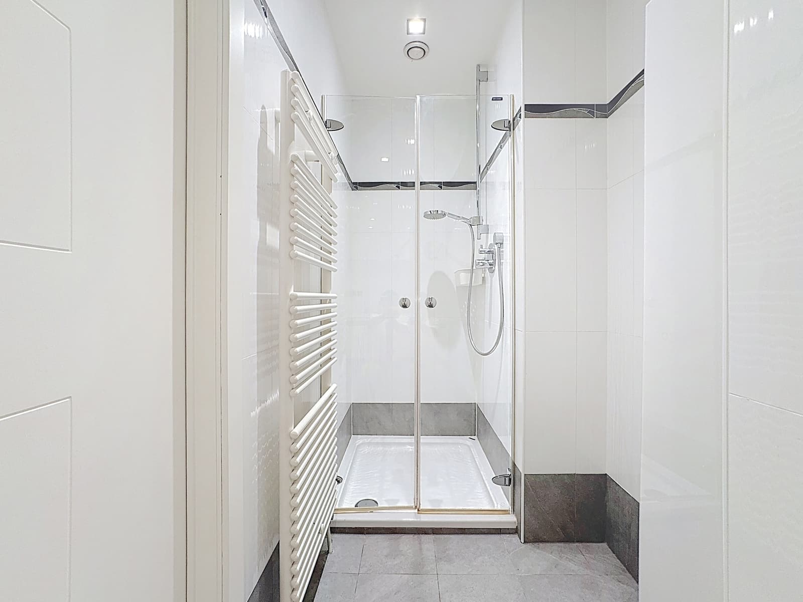 Salle de Bain avec Douche Vitrée – You Real Estate Agency Salle de bain moderne avec douche vitrée et carrelage blanc en appartement.