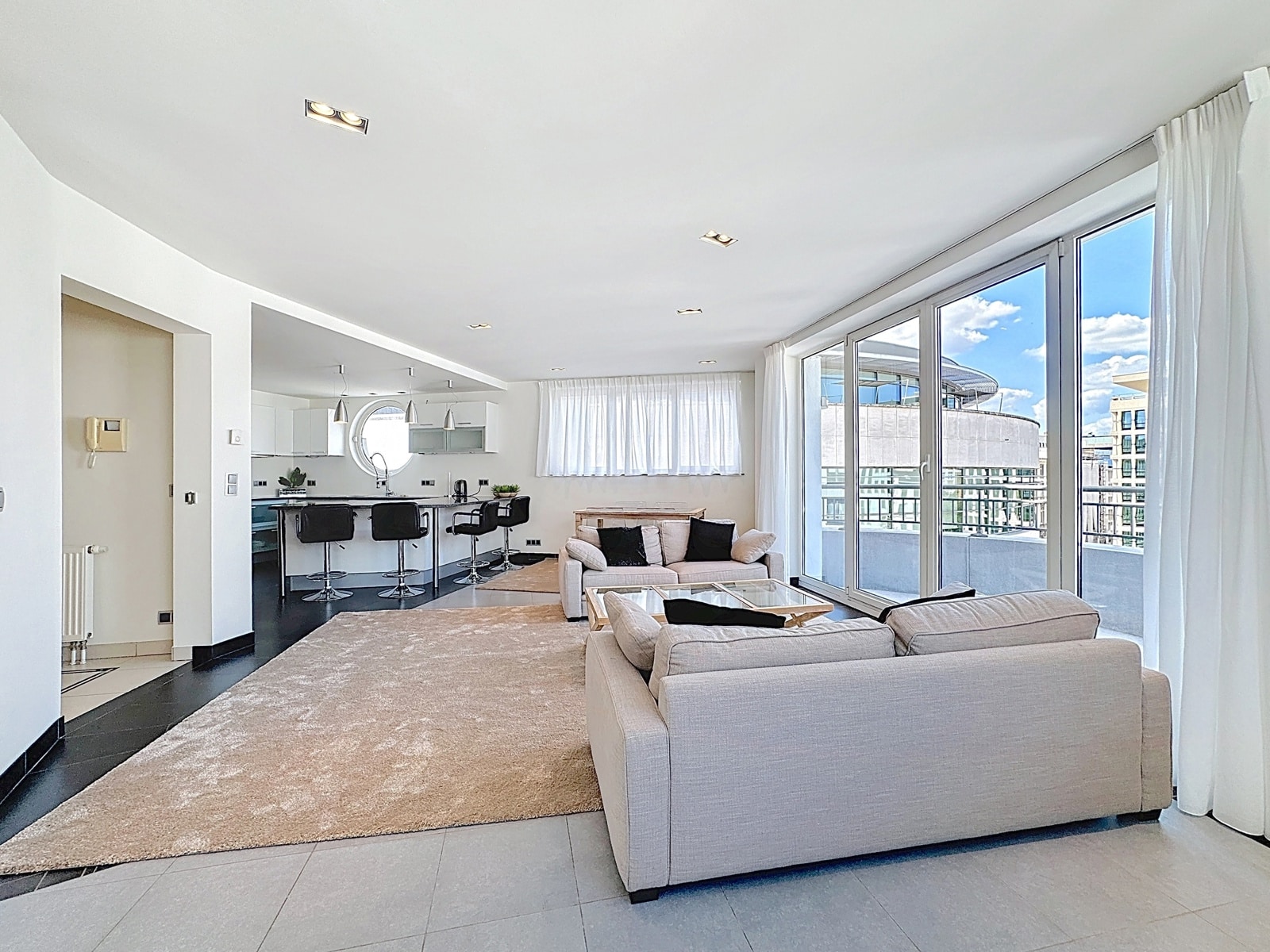Salon Lumineux et Cuisine Ouverte – You Real Estate Agency Appartement lumineux avec salon contemporain, cuisine ouverte et balcon.
