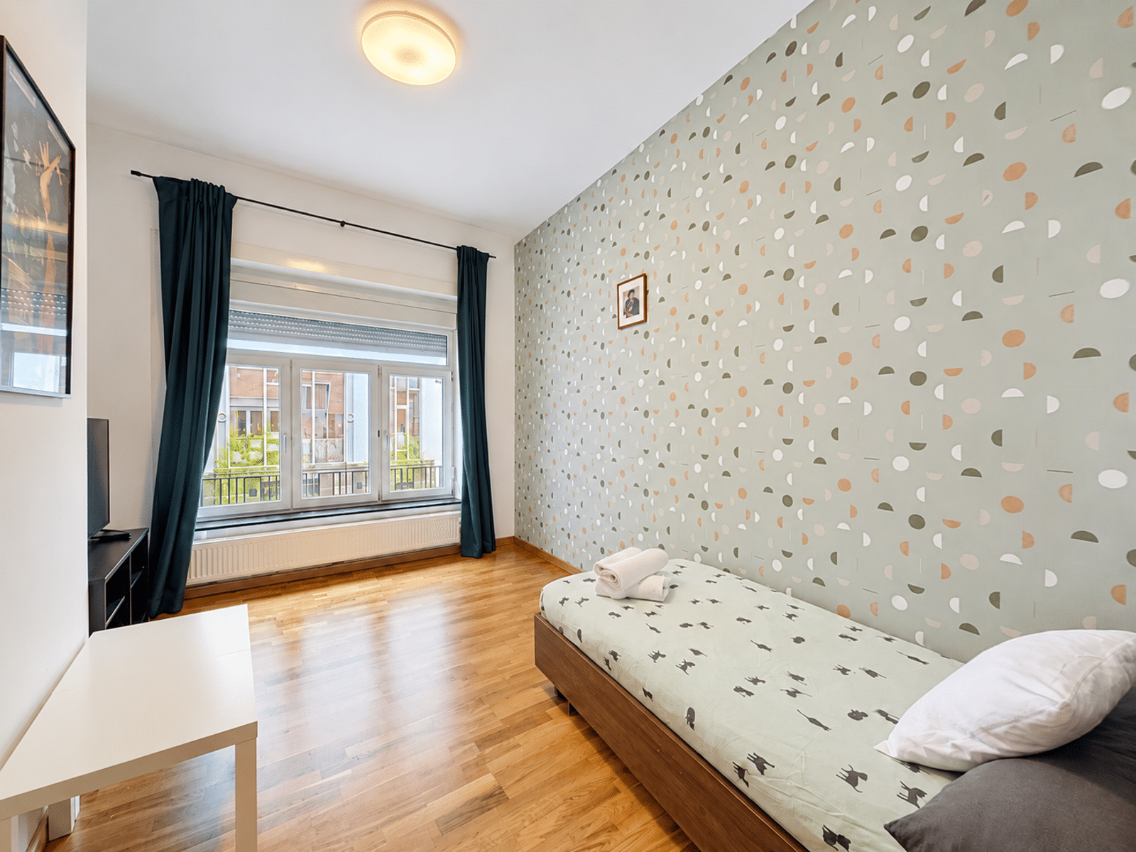 Chambre Lumineuse avec Papier Peint – You Real Estate Agency Chambre lumineuse d’appartement avec lit simple, parquet, papier peint et grande fenêtre.
