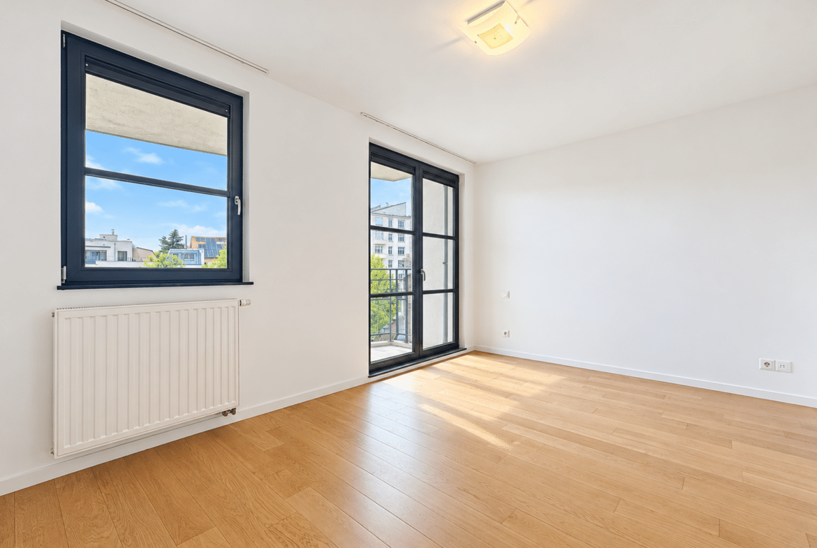 Salon lumineux d’appartement avec parquet, grande fenêtre et balcon.