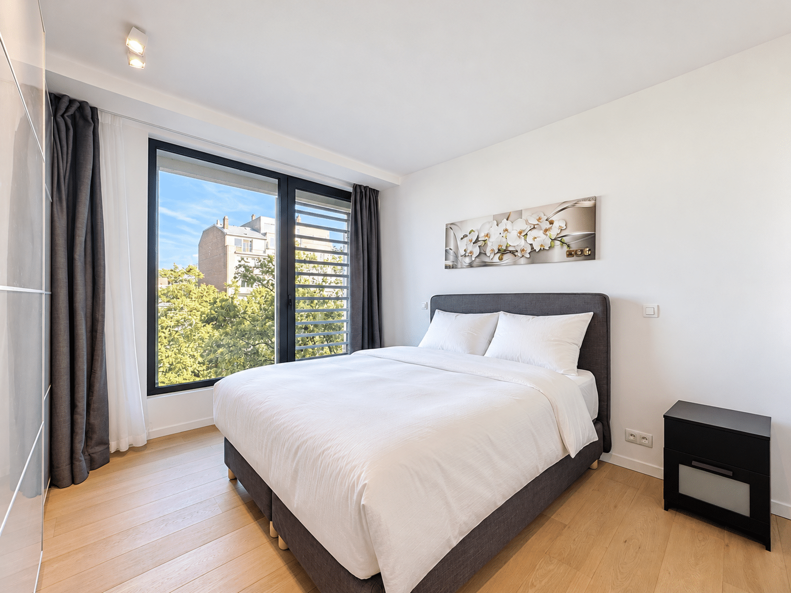 Chambre Lumineuse et Moderne – You Real Estate Agency Chambre lumineuse d’appartement moderne avec parquet et grande fenêtre.