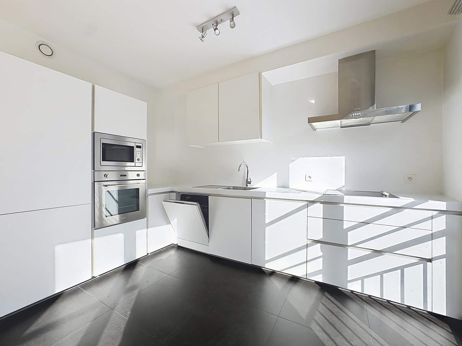 Equipped and Bright Modern Kitchen - You Real Estate Agency Cuisine moderne lumineuse avec rangements blancs et électroménagers intégrés dans appartement neuf.